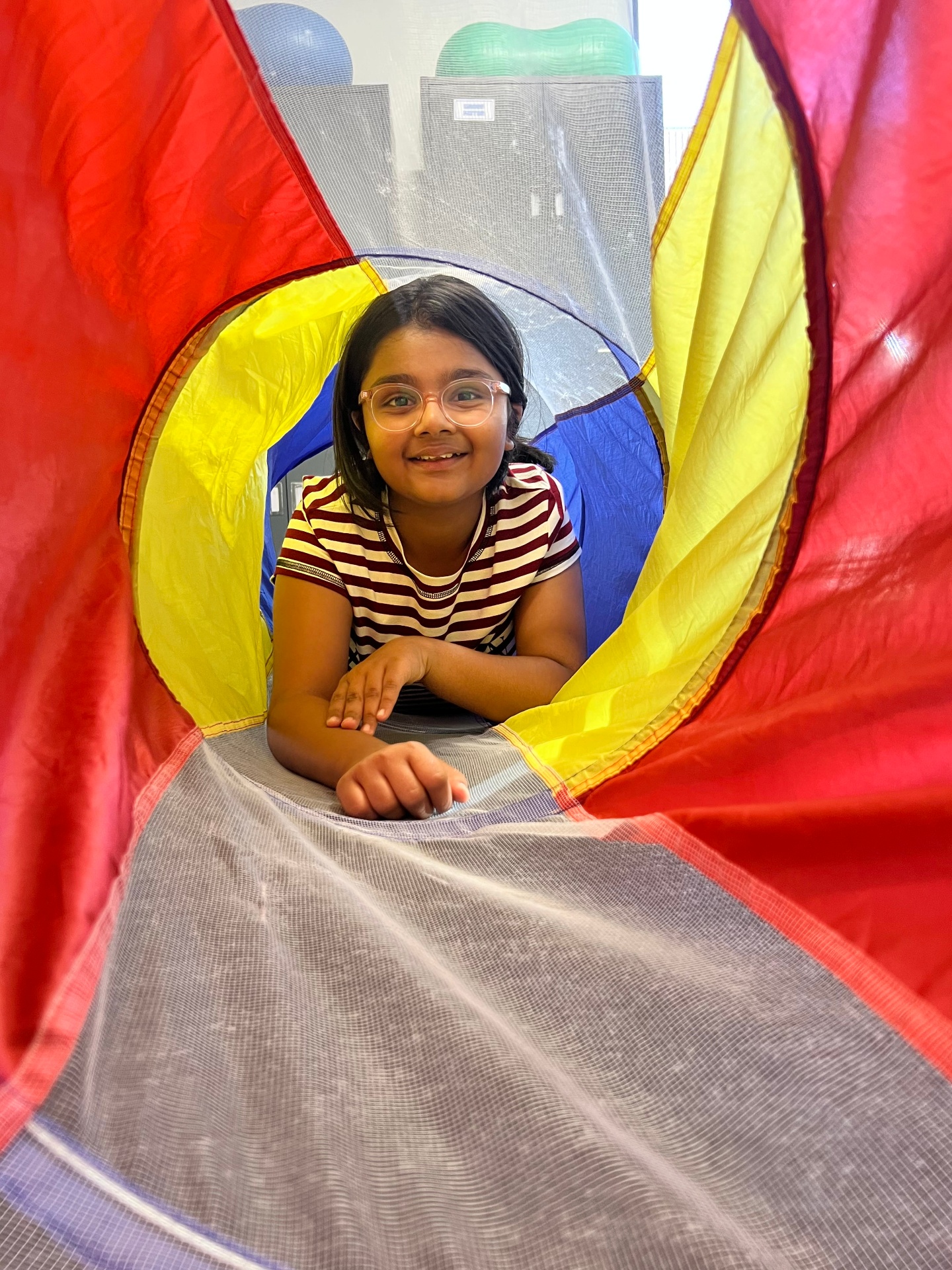 Child smiling while crawling through a colourful tunnel